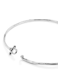 Pulsera de plata con un diseño liso y elegante. Presenta un broche circular y un pequeño acento de gema en un extremo, destacando su estilo minimalista.