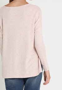 Ljusrosa stickad tröja med bred halsringning och långa ärmar. Baksidan har en något längre nederkant och är gjord av ett mjukt, texturerat tyg.