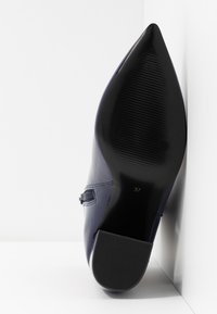 Zapato de charol náutico de tacón alto con punta afilada, con una suela negra texturizada y etiqueta de tamaño 37.