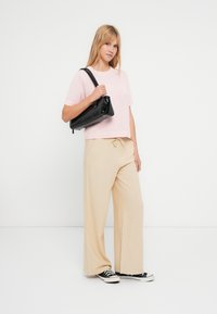 Šviesiai rožinė trumpomis rankovėmis tekstūruota palaidinė, smėlio spalvos platėjančios kelnės ir juoda rankinė. Modelis dėvi juodus sportinius batelius su baltais padais. Paprastas, kasdienis aprangos stilius.