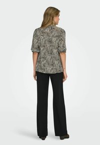 Top de manga corta, con estampado en negro y beige, de corte holgado; combinado con pantalones negros de tiro alto, zapatos planos, textura suave.