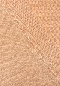 Pfirsichfarbener Strickstoff mit einer glatten Textur und gerippten Details an den Kanten, die einen subtilen Glanz betonen.