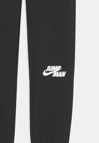 Schwarze Sweatpants mit einem weißen "JUMP MAN" Logo am linken Bein, aus glattem Stoff gefertigt, mit geradem Beinschnitt und elastischem Bund.