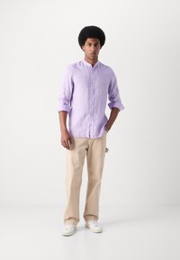 Lichtpaarse lange mouwen shirt met een kraag, opgerolde mouwen; gecombineerd met beige broek en witte sneakers. Eenvoudig ontwerp, geen patronen.
