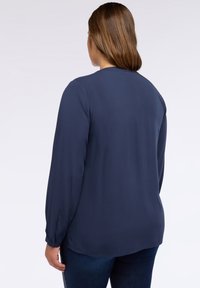 Blusa de manga larga marinera hecha de una tela suave, con un escote redondo y puños abotonados, y un dobladillo recto en la parte posterior.