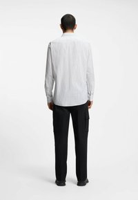 Langærmet skjorte med hvide og grå striber, der har en spids krave og en lige kant, kombineret med sorte cargobukser.