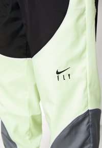 Die Nike FLY-Hosen verfügen über ein Farbblockdesign mit schwarzen, hellgrünen und grauen Panele, die aus leichtem Material mit einer strukturierten Oberfläche bestehen.
