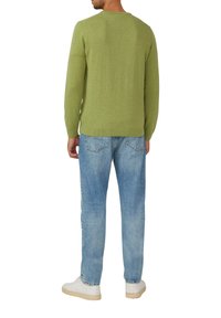 Grüner Strickpullover mit Rundhalsausschnitt, kombiniert mit hellblauen Jeans. Weiße Sneaker auf einer glatten Oberfläche. Keine auffälligen Muster oder Logos sichtbar.