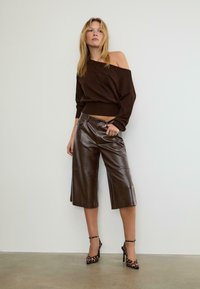 Hnedý sveter s odhalenými ramenami skombinovaný s lesklými hnedými koženými culottes. Model má na sebe leopardie vzorované opätky. Hladká textúra, skrátený strih.