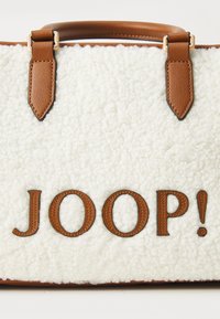 Hvid shearling håndtaske med brune læderdetaljer, udstyret med prægede 'JOOP!' logo i brun. Korte læderhåndtag fastgjort med metalbeslag.