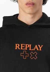 Czarna hoodie wykonana z bawełny, z pomarańczowym logo "REPLAY" i geometrycznymi symbolami z przodu, z kapturem na sznurki i teksturowanym materiałem.