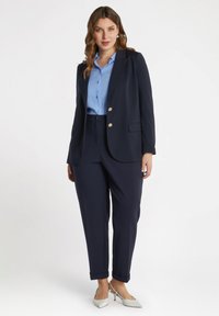Blazer bleumarin cu nasturi aurii, asociat cu o cămașă bleu deschis și pantaloni bleumarin. Pantofii sunt gri deschis, cu vârf și toc ascuțit.