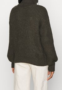 Maglione lavorato a maglia verde scuro con collo alto, texture a coste e maniche ampie. La parte posteriore presenta una vestibilità morbida e un design senza cuciture.