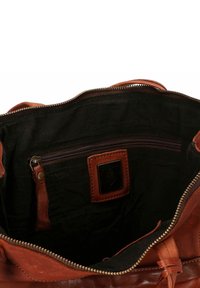 Interno di una borsa in pelle marrone con fodera in tessuto nero, dotato di una tasca con zip e un'etichetta in pelle beige con un logo a forma di ancora.