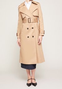 Beige trenchcoat med dubbelknäppt knappar, skärp i midjan, axelklaffar, sidfickor och en strukturerad silhuett.