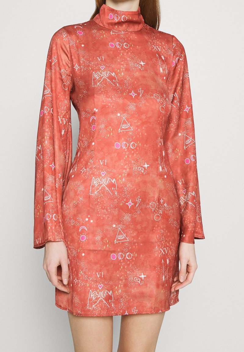 Robe mini corail à manches longues avec col montant, ornée de symboles mystiques blancs, flèches, étoiles, lunes et motifs de gestes de la main sur le tissu.