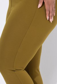 Olivgröna leggings gjorda av en stretchig tyg, med en slät textur och en åtsittande design med en sömdetalj längs sidan.