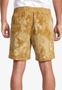 Tan corduroy shorts with a tie-dye pattern, featuring an elastic waistband and a relaxed fit, shown from the back.