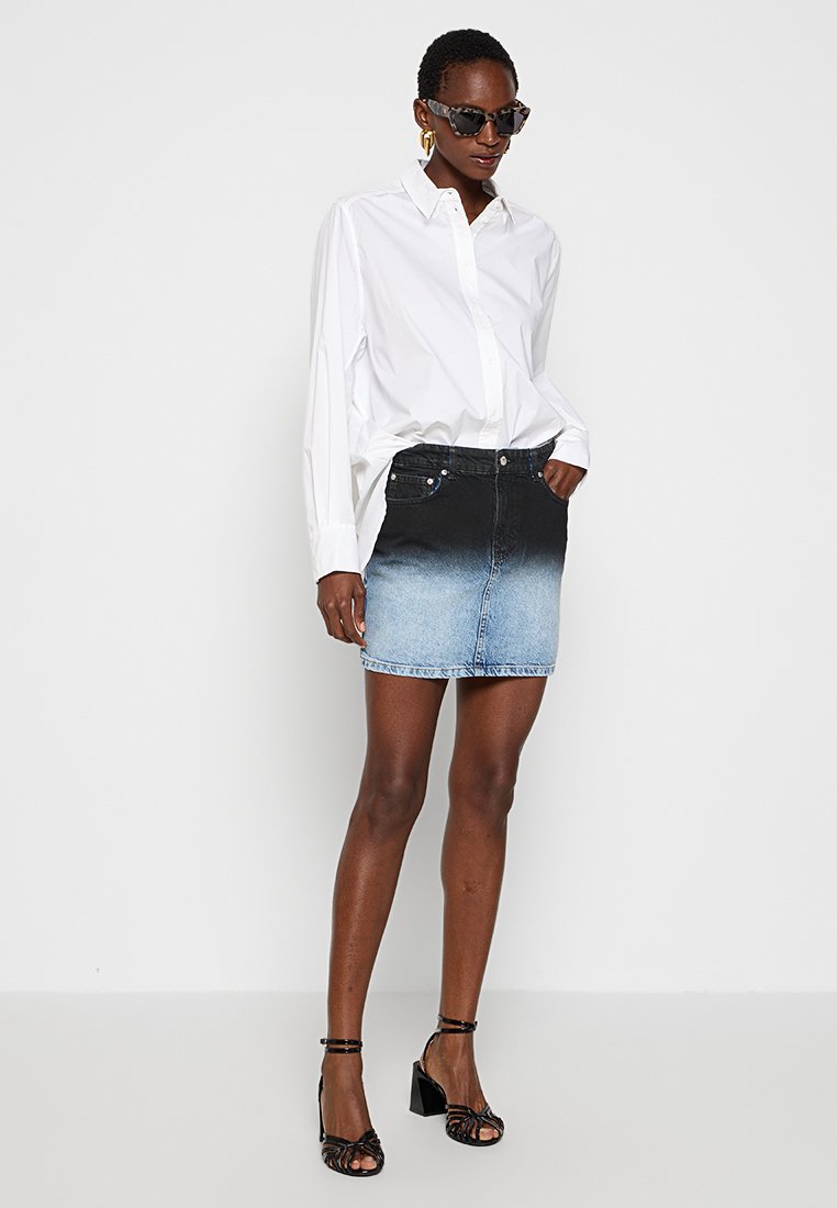 Denim rok met een ombre-effect, die overgaat van zwart naar lichtblauw. Heeft een aansluitend ontwerp en vijf zakken, gedragen met een wit shirt.
