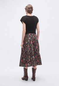 Czarny krótki top z krótkim rękawem zestawiony z długą, wzorzystą spódnicą w kolorowe kwiatowe wzory oraz falbaniastym dołem, noszony z brązowymi butami.