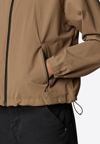 Brown lightweight jacket with elastic cuffs, a zippered front, and drawstring hem; textured fabric and black zipper accents.