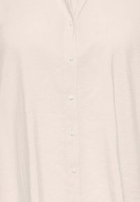 Hellbeiges Leinenhemd mit durchgehender Knopfleiste, kleinen, runden Knöpfen und legerer Passform. Weiche Textur mit minimalen Falten.