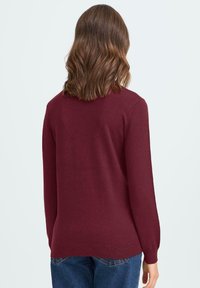 Bordo pleteni pulover s dugim rukavima, okruglim izrezom i opuštenim krojem, sa rebrastim rubom i manžetama. Materijal izgleda glatko s minimalnom teksturom.