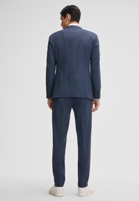 Completo blu navy con una trama testurizzata, dotato di uno spacco singolo e una vestibilità sartoriale. Abbinato a sneaker bianche per un contrasto informale.