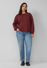 Bordeaux kleurige sweatshirt met lange mouwen, ontspannen pasvorm en geribbelde manchetten, gecombineerd met lichtblauwe rechte jeans en donkere schoenen. Duidelijk, eenvoudig ontwerp.