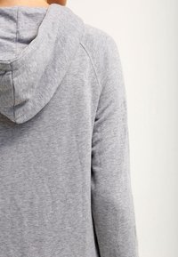 Sudadera de color gris claro con una tela suave y texturizada. Presenta una capucha amplia y mangas raglán para mayor libertad de movimiento. Diseño minimalista.