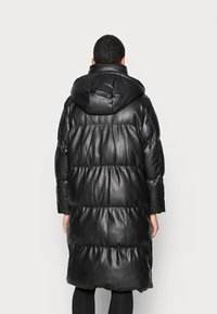 Černý prošívaný kabát s kapucí, dlouhými rukávy a prošíváním. Vyrobený ze syntetické kůže s hladkou texturou a volným střihem.