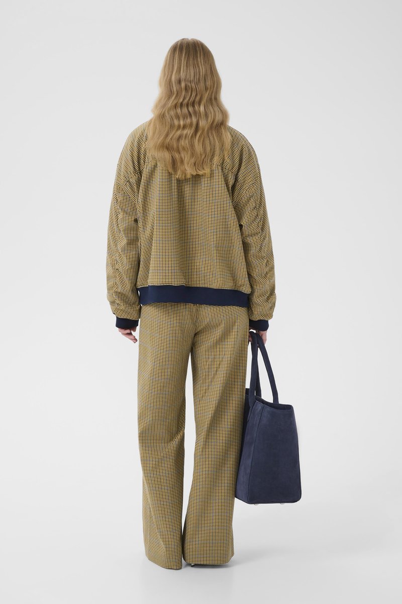 Quilted yellow and navy checkered jacket paired with matching wide-leg trousers; holding a blue suede tote bag.