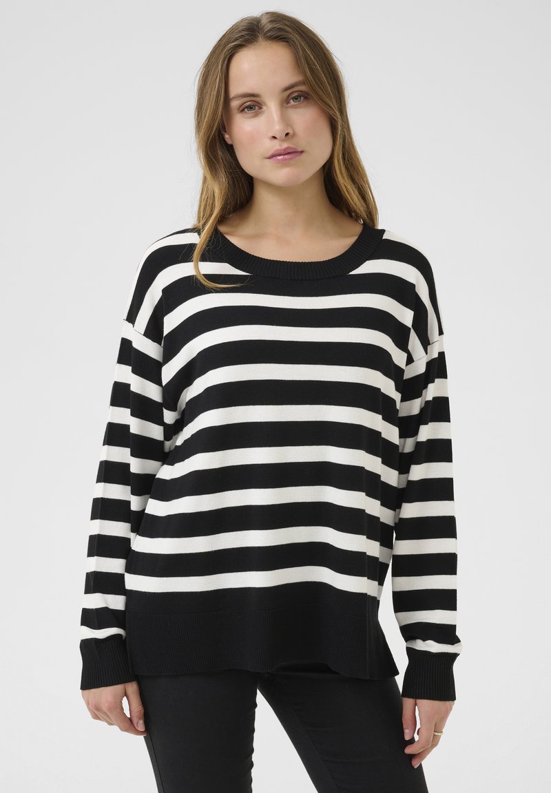 Pull rayé noir et blanc avec un col large, des manches longues et des poignets côtelés. Texture douce, coupe décontractée et ourlet légèrement plus long à l'arrière.
