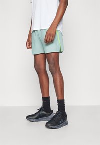 Μέντα αθλητικά σορτς με φωσφοριζέ πράσινη λωρίδα στο πλάι, σε συνδυασμό με μαύρα αθλητικά παπούτσια και μαύρες κάλτσες μέχρι τον αστράγαλο. Απλός και λειτουργικός σχεδιασμός.