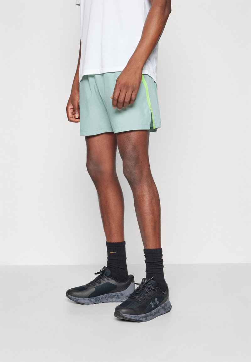 Μέντα αθλητικά σορτς με φωσφοριζέ πράσινη λωρίδα στο πλάι, σε συνδυασμό με μαύρα αθλητικά παπούτσια και μαύρες κάλτσες μέχρι τον αστράγαλο. Απλός και λειτουργικός σχεδιασμός.