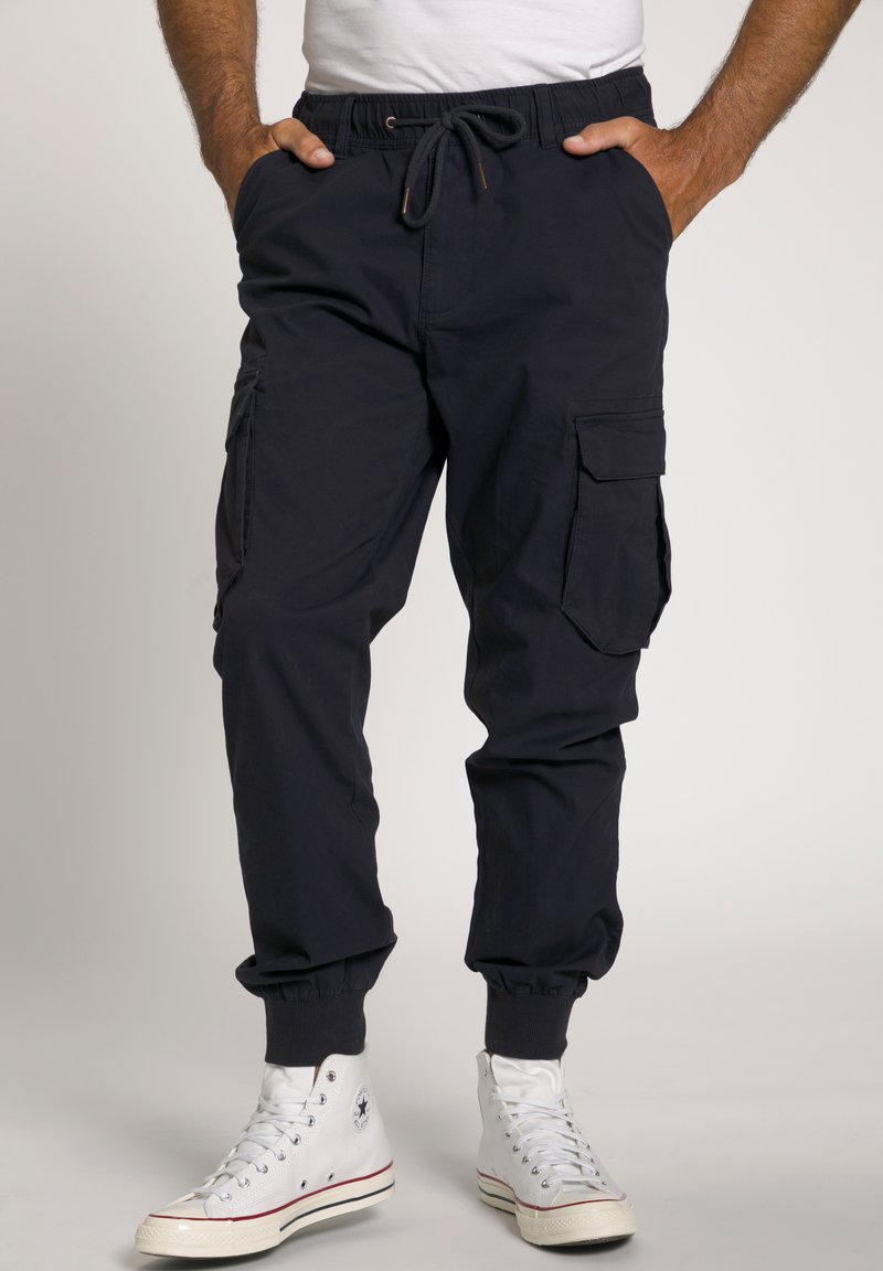 Marine cargobroek met elastische tailleband, trekkoord en meerdere zakken. Boorden zijn afgewerkt met elastische trim. G dragen met witte high-top sneakers.