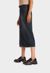 Gonna midi in denim blu scuro, presenta un design a taglio dritto e tasche. Abbinata a mocassini lucidi marrone scuro su una suola spessa.