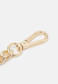 Mousqueton en métal doré attaché à des maillons de chaîne, gravé "MICHAEL KORS" sur le côté.