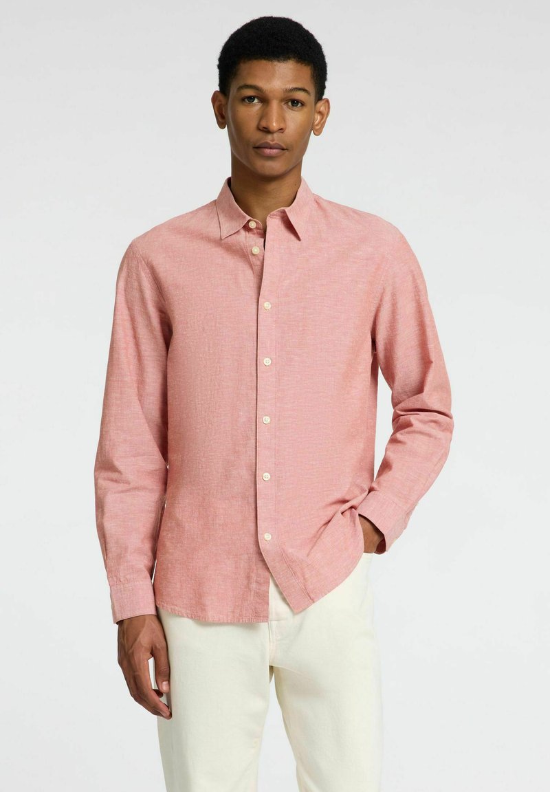 Camisa de botón de color rosa claro con una tela texturizada, de mangas largas y un cuello clásico, combinada con pantalones de color claro.