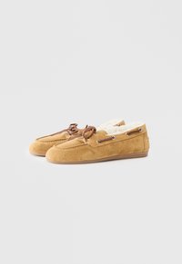 Suede moccasin slippers in tan with a soft inner lining. Features leather laces and metal eyelets. Smooth sole for indoor use.