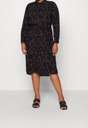 Woman wearing a black long-sleeve midi dress with abstract beige line patterns and black open-toe heeled sandals.