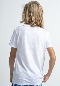 Bílý tričko s krátkým rukávem vyrobené z texturované tkaniny, s kulatým výstřihem a ohrnutými rukávy, viděné zezadu.