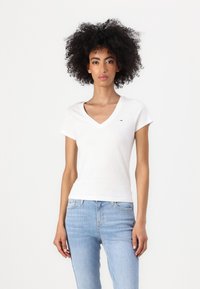 Hvit kortermet v-hals t-skjorte i mykt bomullsmateriale, med en liten logo på brystet, sammen med lyseblå denimjeans.