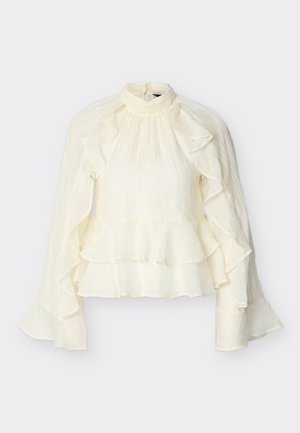 Μπλούζα κρεμ με ψηλό γιακά και μακριά μανίκια, με βολάν κατά μήκος των μανικιών και του τελειώματος, από υφή και ελαφρύ ύφασμα.