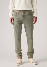 Világos zöld farmernadrág egyenes szabással, öt zsebbel és gombos cipzárral. Off-white sportcipővel és textúrázott fehér felsővel párosítva.