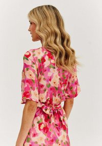 Květinové šaty v odstínech růžové, červené a zelené s krátkými rukávy a detailem na zavázání vzadu. Měkká, lehká tkanina s hladkou strukturou.