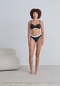 Černá podprsenka s nastavitelnými ramínky a odpovídajícími vysokými bikinovými kalhotkami. Hladký povrch, minimalistický design s kontrastním pasem.