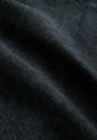 Ciemnoniebieska tkanina denimu o gładkiej teksturze, z delikatnymi wzorami skośnymi i lekkim połyskiem, ukazująca łagodne zagniecenia i swobodny układ.