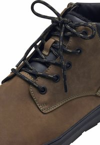 Brown leather boot with black textile accents, round laces, metal eyelets, and contrasting stitching. Smooth texture and durable sole design.