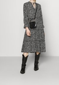 Abito a righe in bianco e nero con gonna a strati e maniche lunghe, abbinato a una piccola borsa a tracolla nera e stivali da cowboy neri.